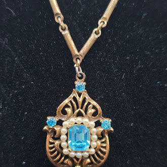 Gold tone filigree pendant necklace with blue crystal and faux pearl frame